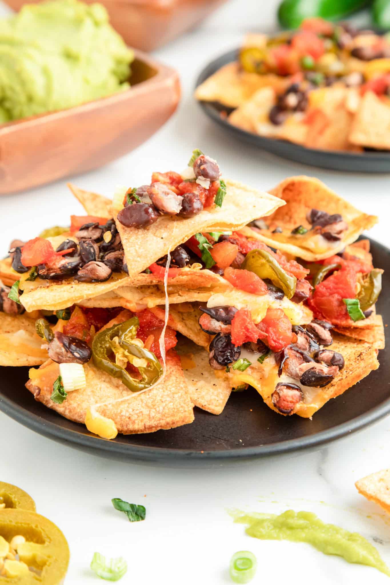 stack of cooked nachos topped with black beans, salsa, jalapeños, and cheese.