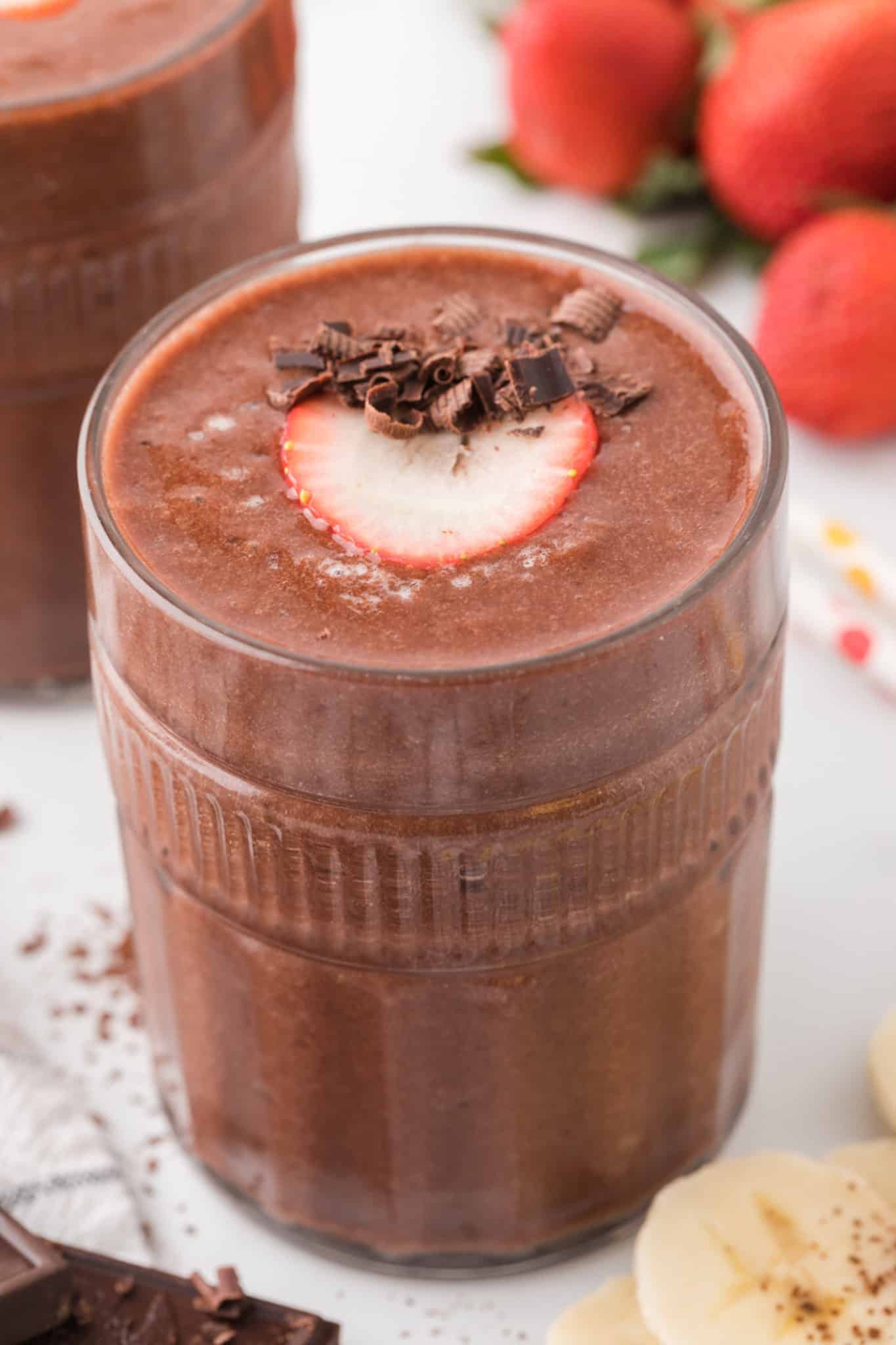 ingredients for chocolate strawberry banana smoothie in a glass with chocolate shavings on top.