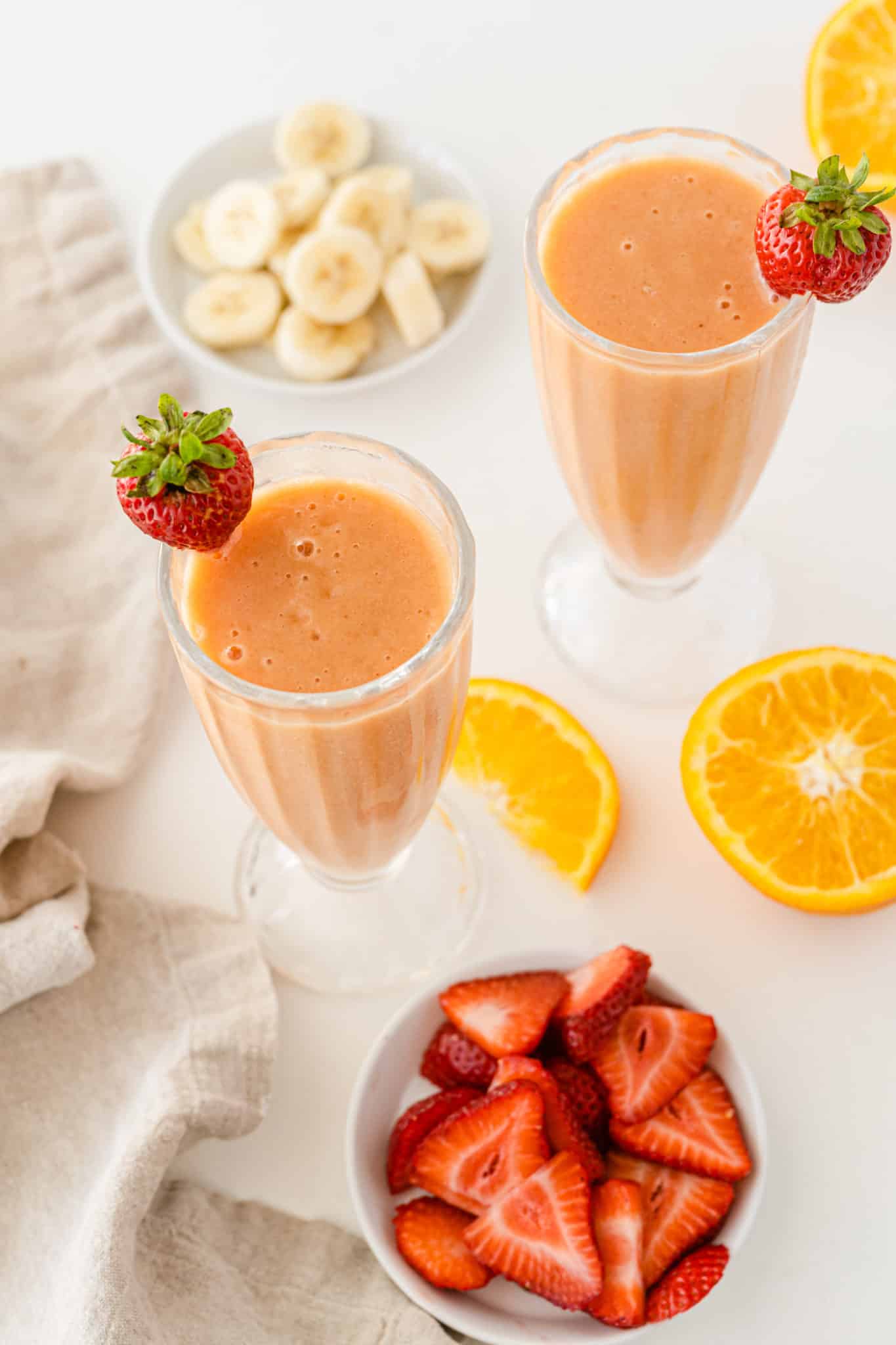 two glasses of strawberry mango smoothie on table with ingredients.