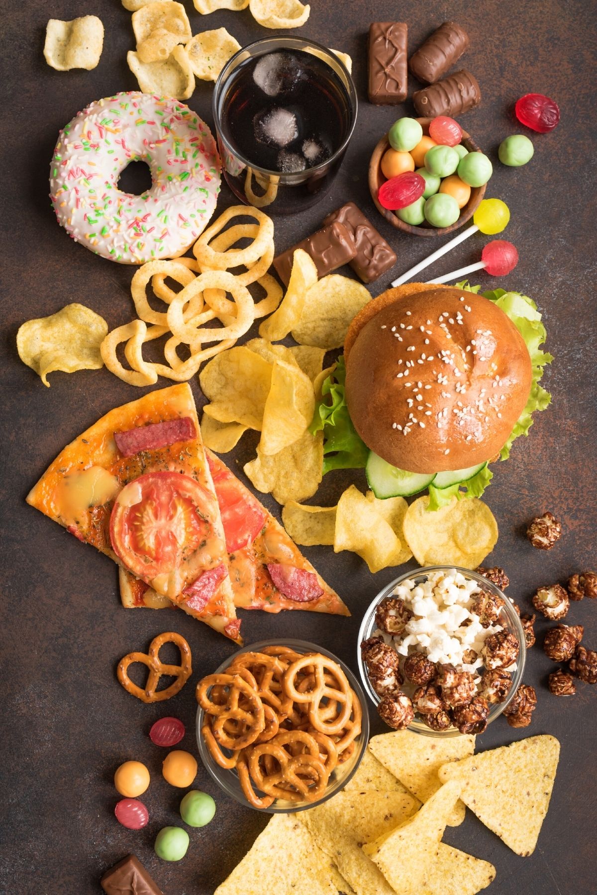 A hamburger, pizza slices and candy on a table. 