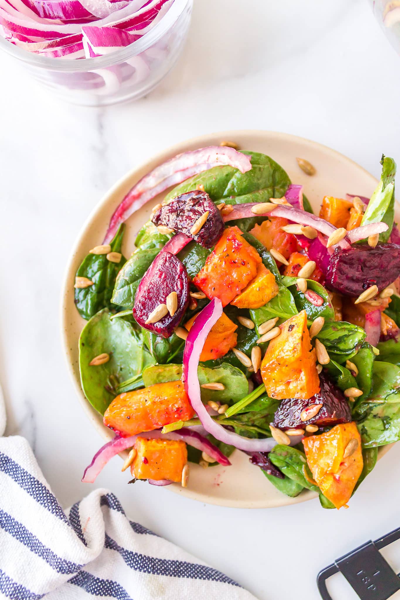 Close up of diced beets and sweet potatoes on a dressed spinach salad.
