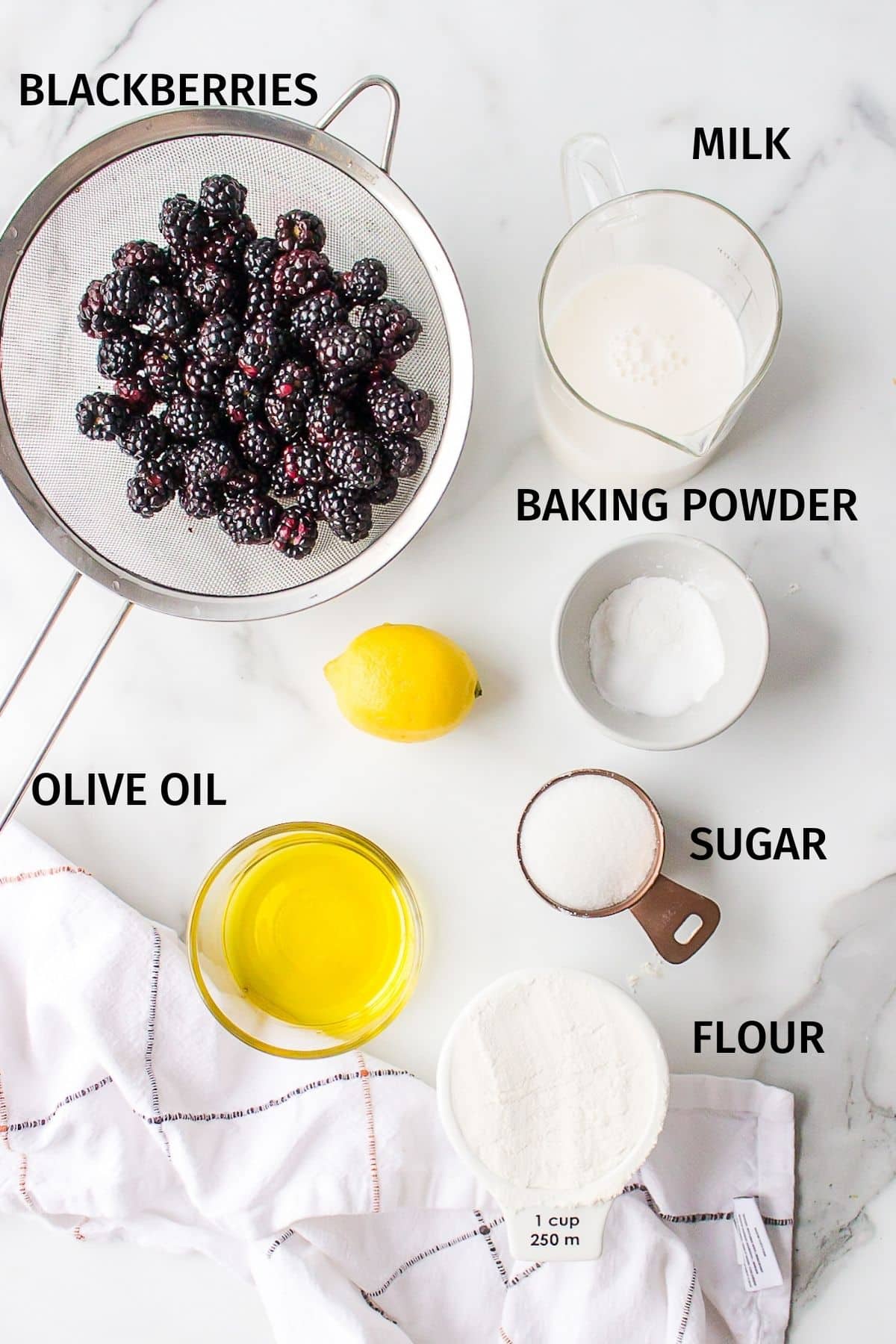 Ingredients for vegan blackberry muffins in small bowls on a white surface.