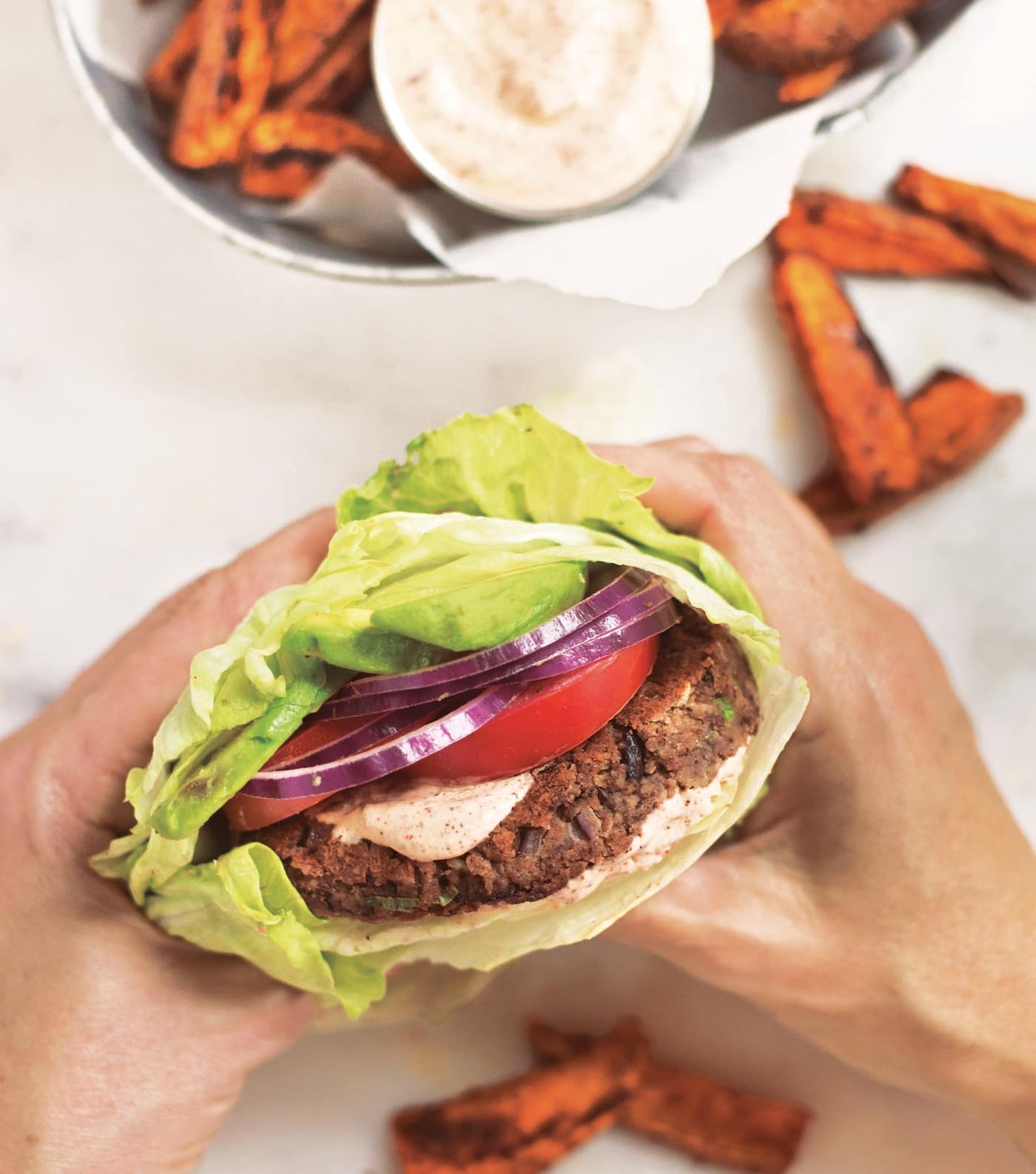 person holding a gluten-free black bean burger wrapped in lettuce.