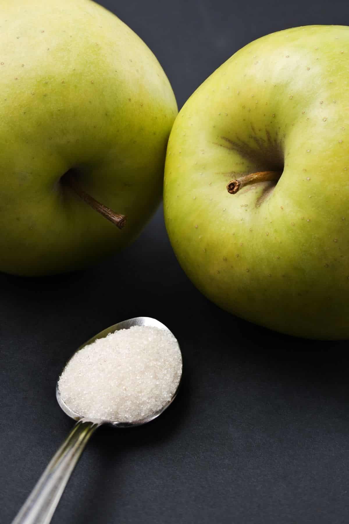 A spoon of sugar in front of 2 apples.