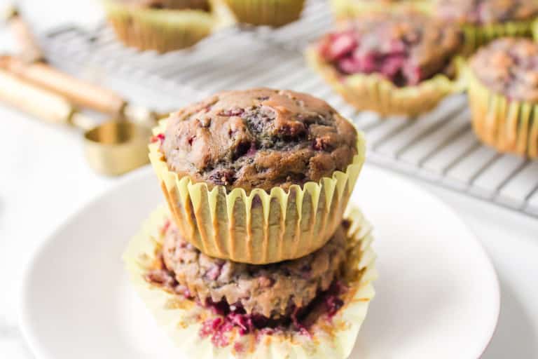 Two vegan blackberry muffins in yellow wrappers stacked on a white plate.