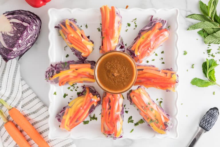 Veggie summer rolls on a platter with a bowl of peanut sauce.