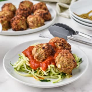A plate of zoodles and turkey meatballs with serving dishes in the background.