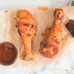 Two air fried BBQ chicken drumsticks on a sheet of parchment paper.
