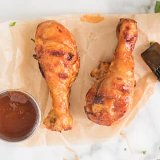 Two air fried BBQ chicken drumsticks on a sheet of parchment paper.