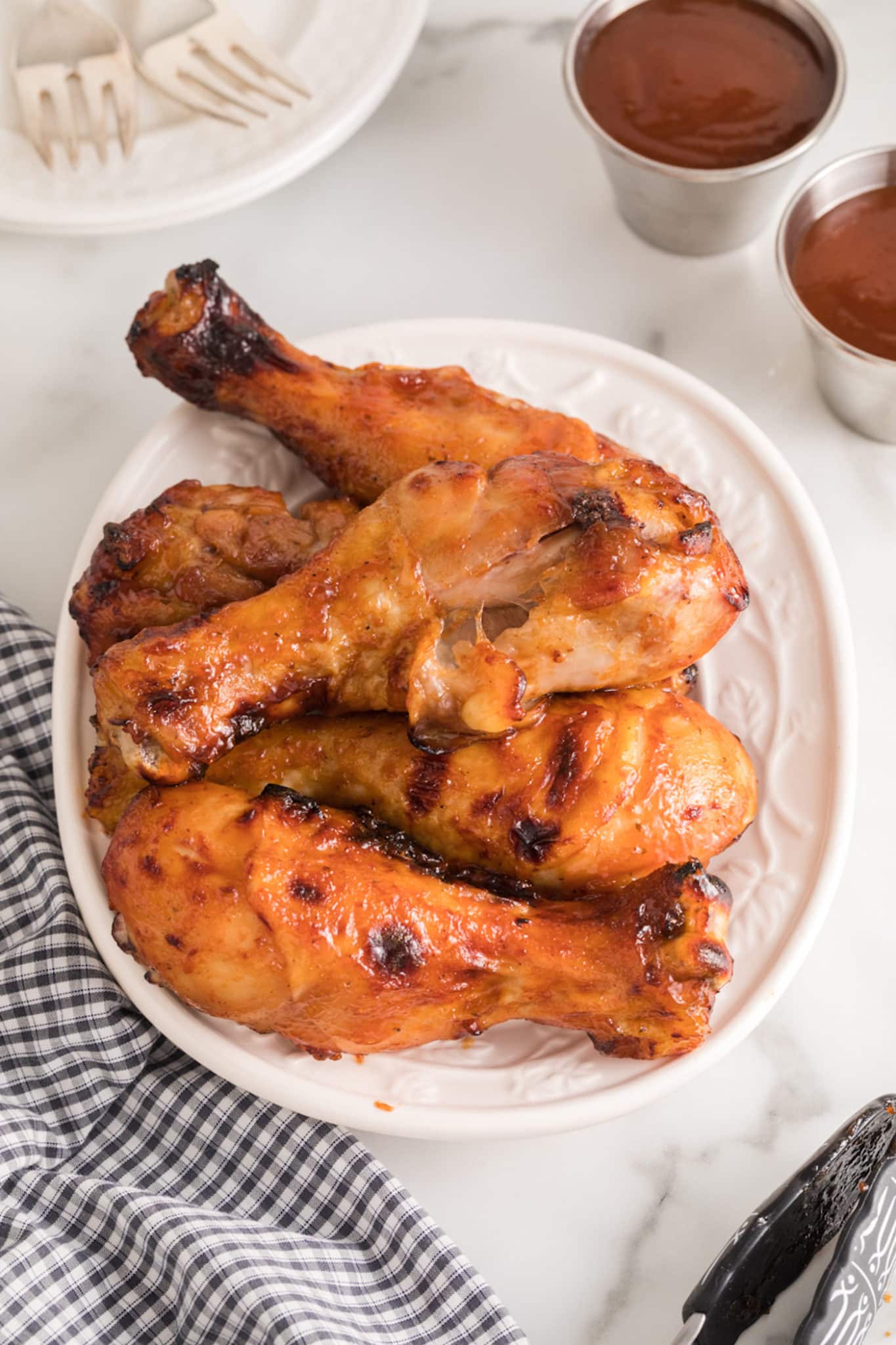 Air fryer BBQ chicken legs piled up on a white plate.