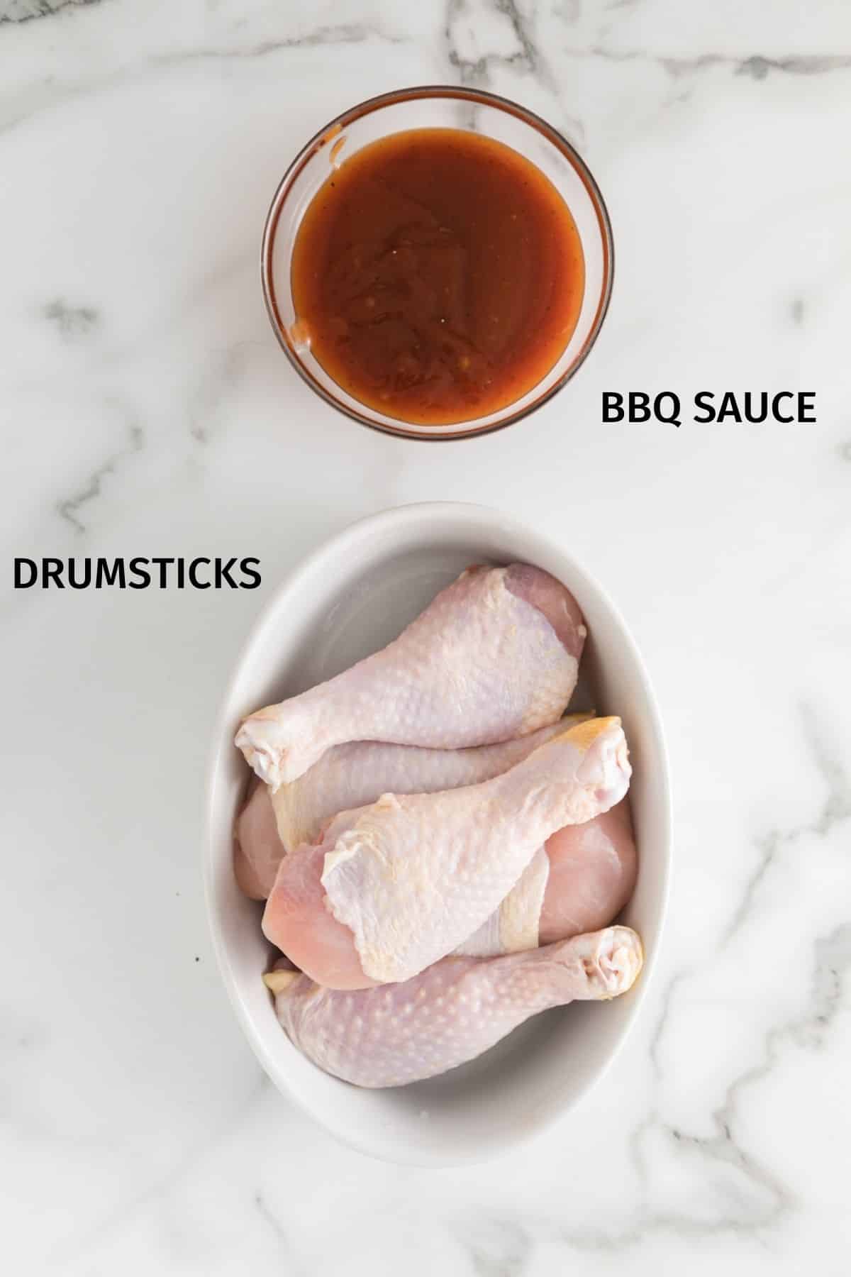Chicken drumsticks and BBQ sauce in bowls on a white surface.