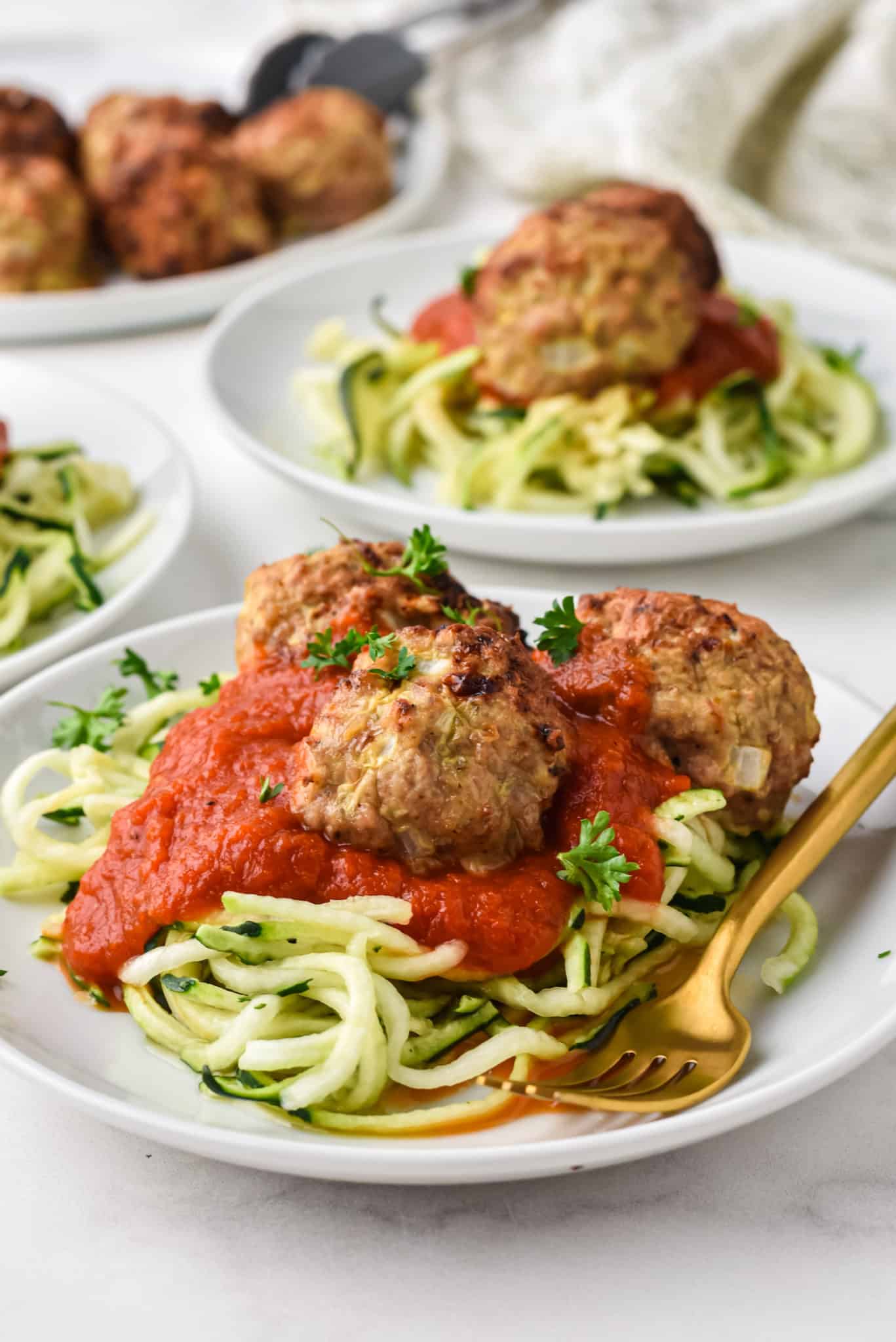 Three plates of zoodles have been topped with red sauce and turkey meatballs.