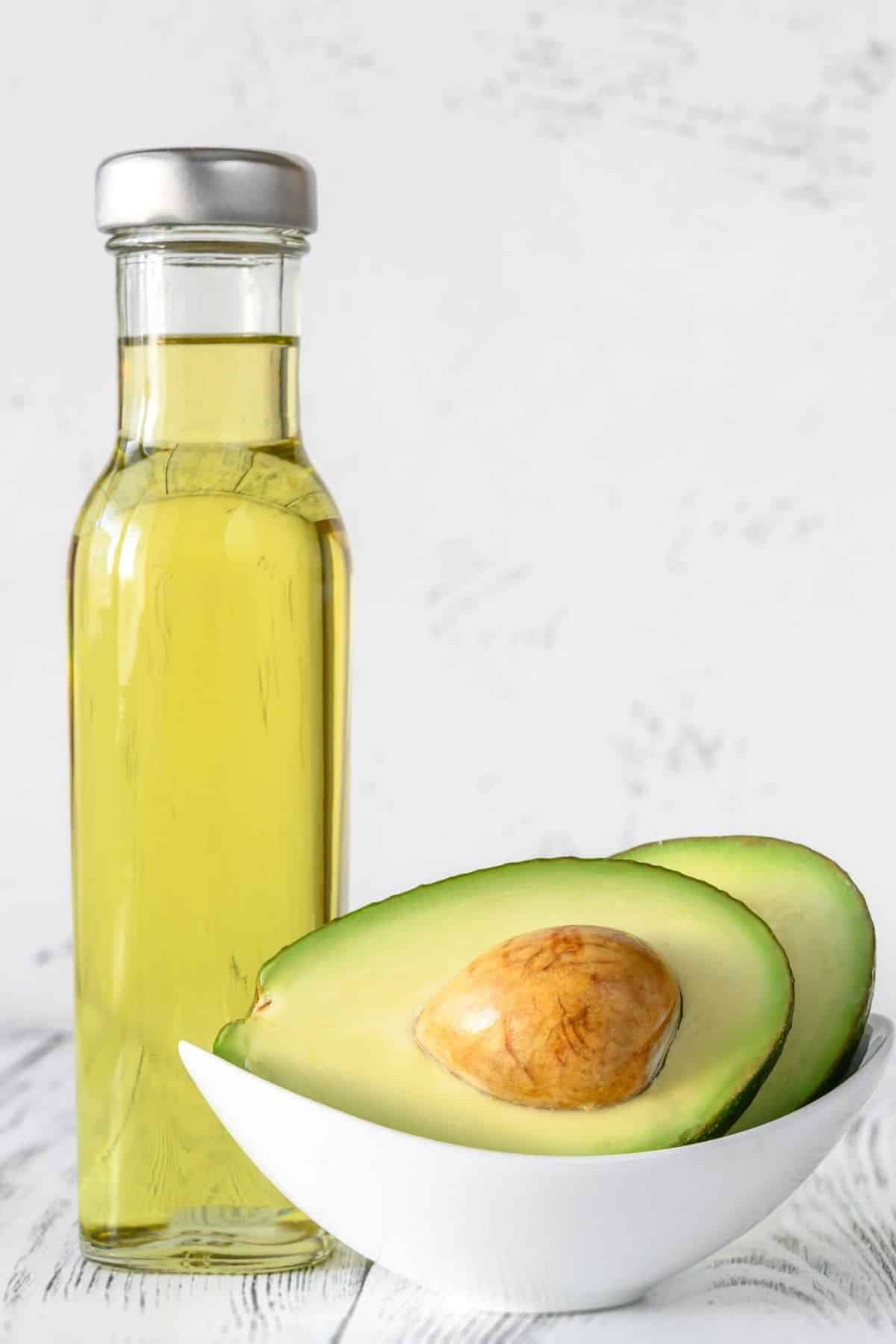 Jar of avocado oil next to a halved avocado.