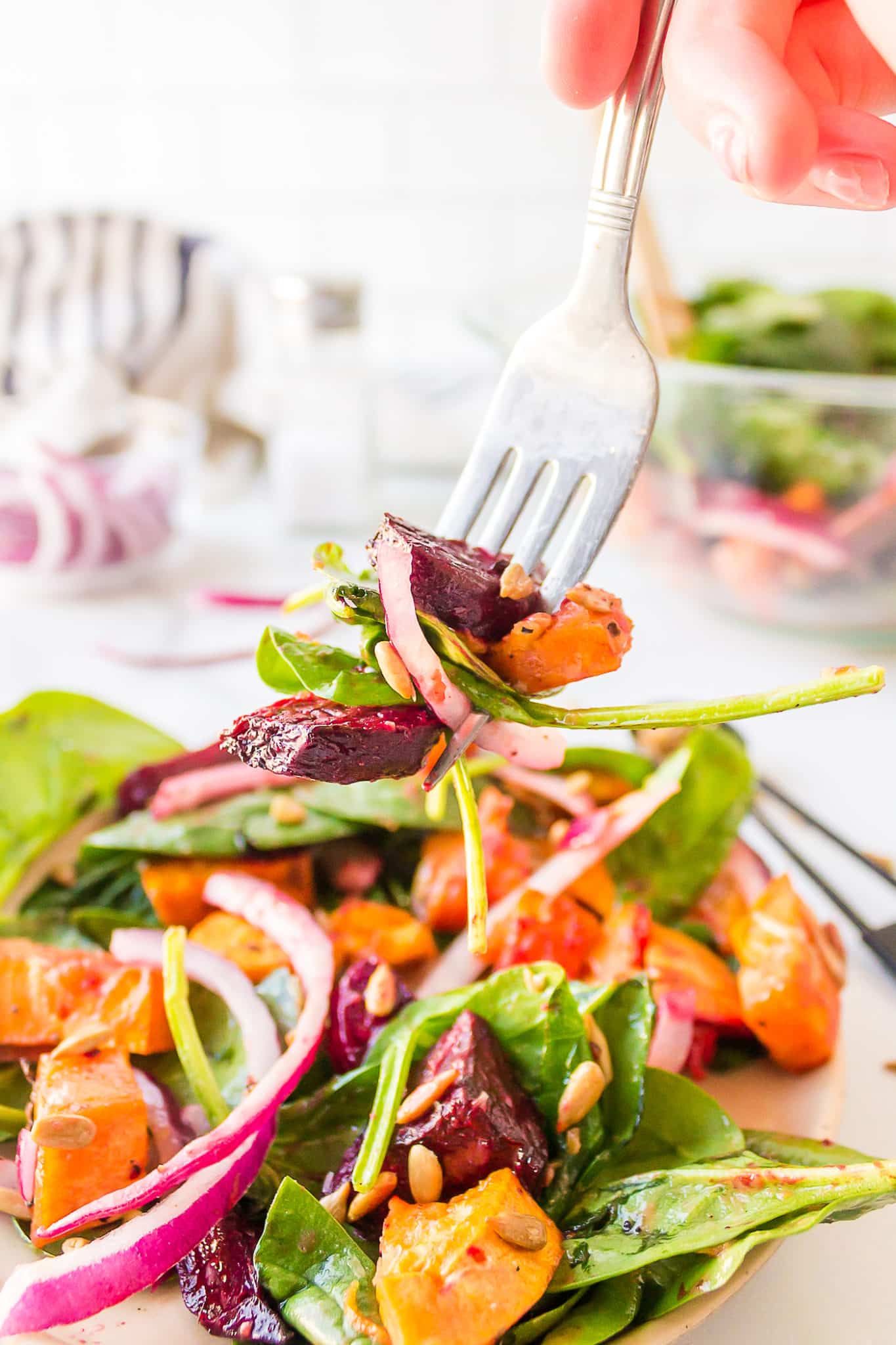 A fork picking up a bite of beet and sweet potato spinach salad.