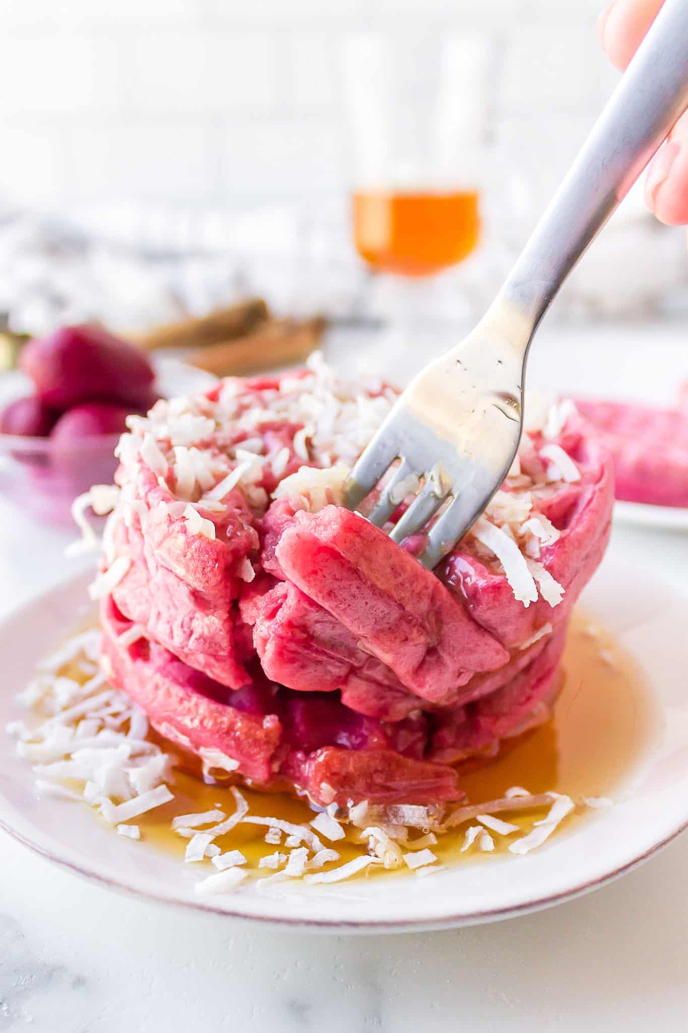 A fork picking up a bite of pink waffles from a syrup coated stack.