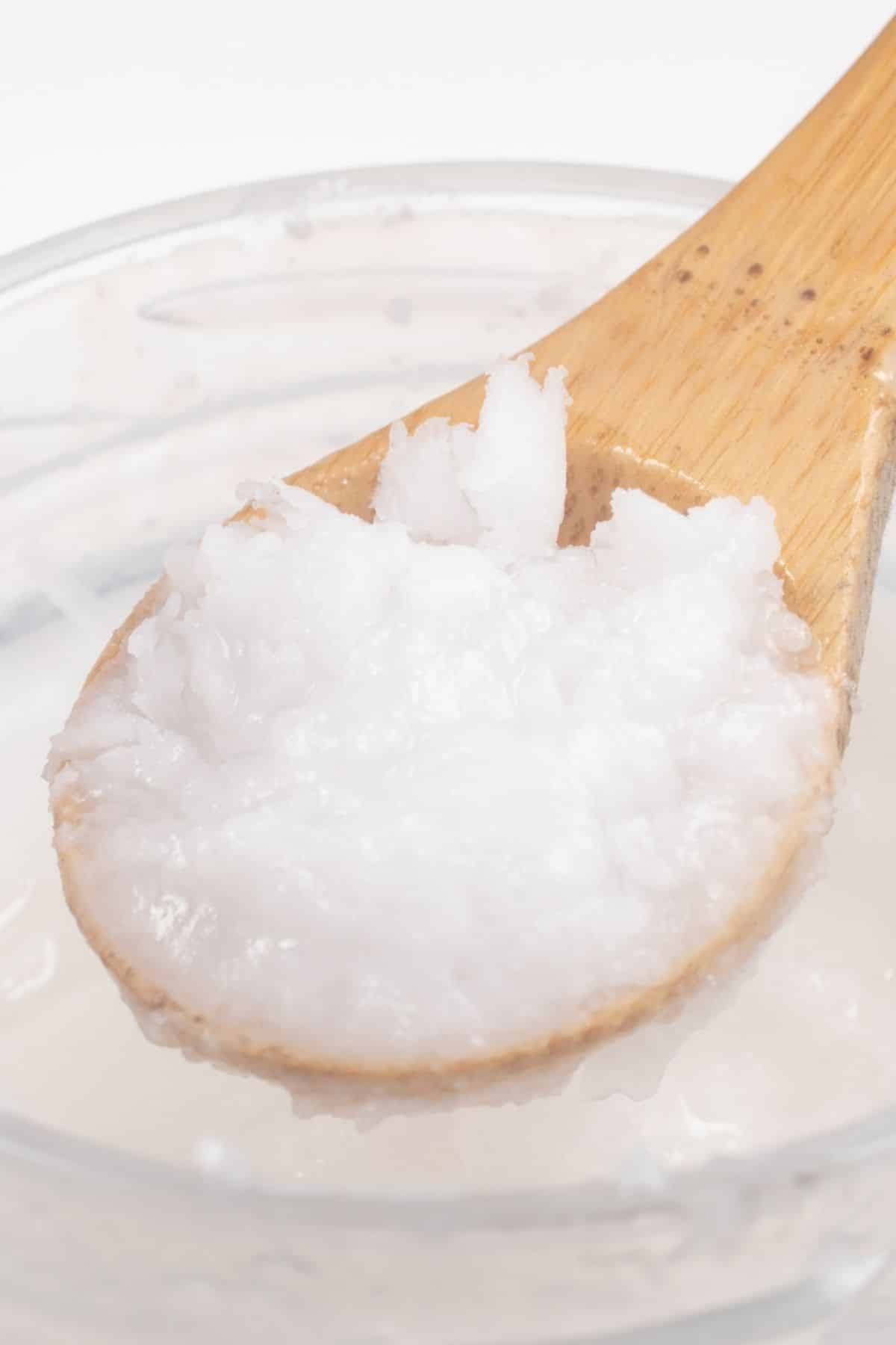 Coconut oil in a wooden spoon over a jar.