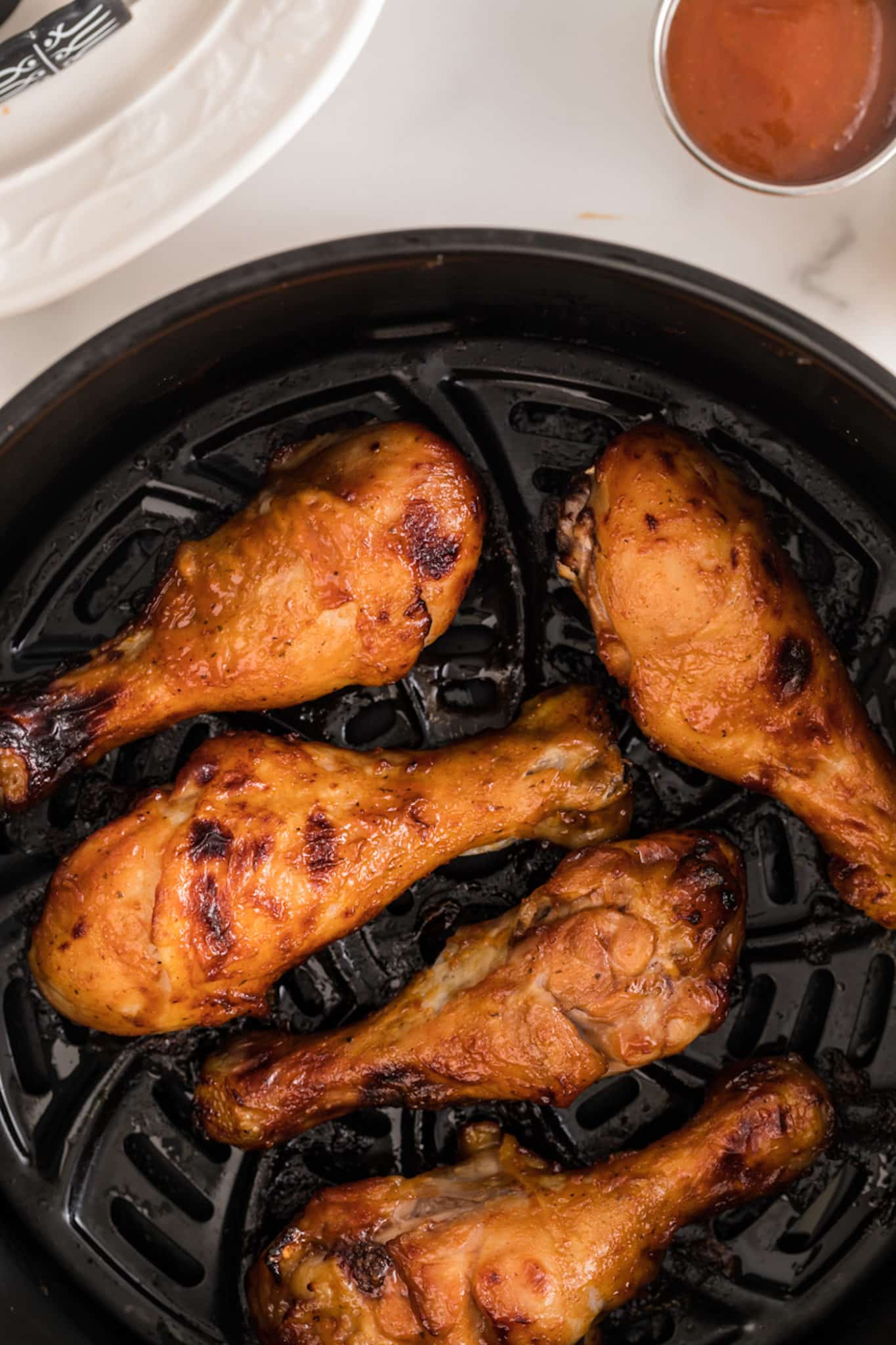 Cooked BBQ drumsticks in the basket of an air fryer.