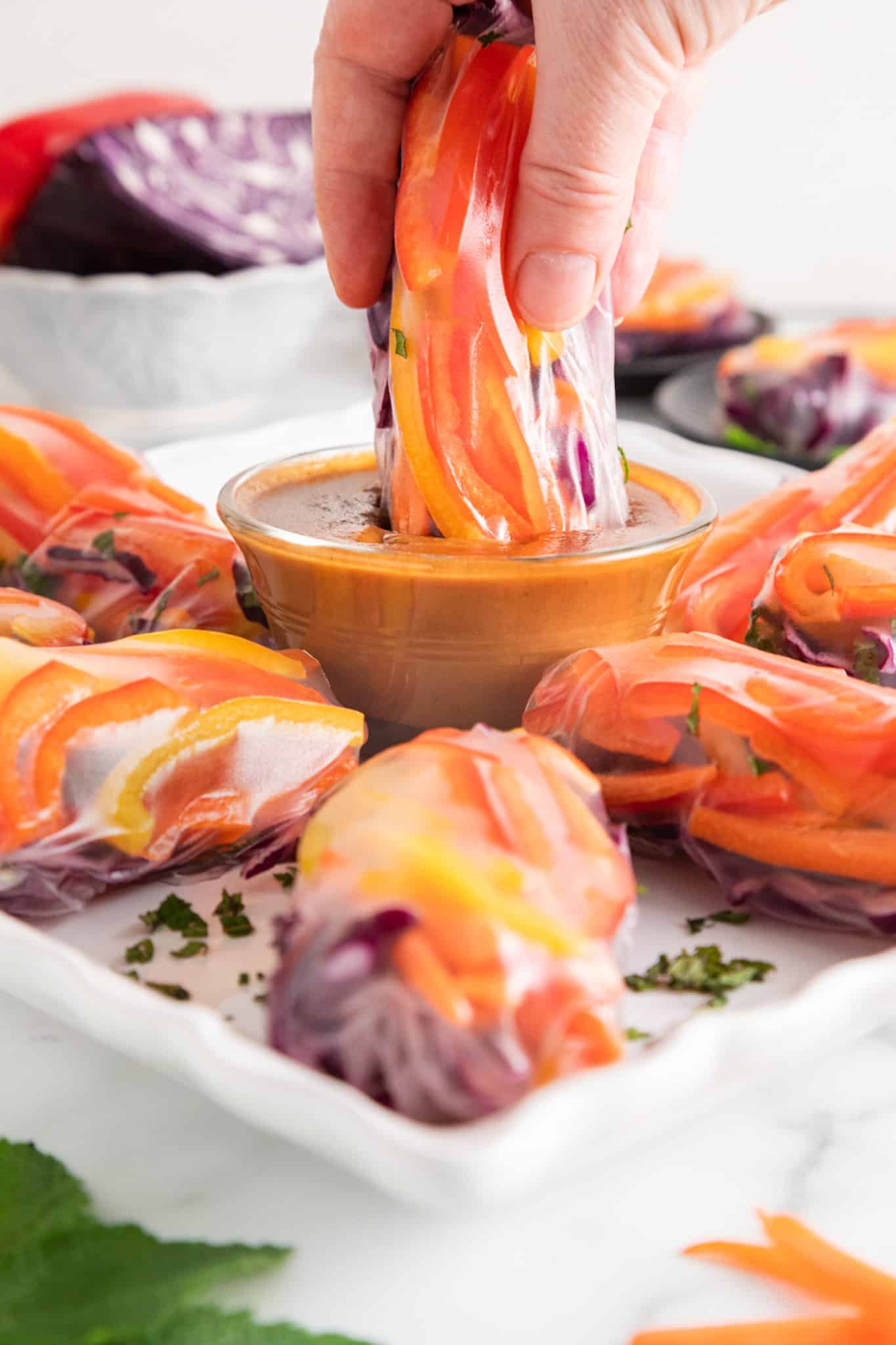 A vegan summer roll being dipped into a bowl of peanut sauce.