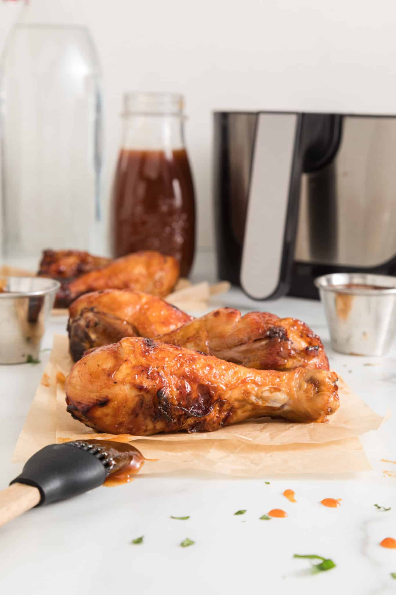 BBQ chicken drumsticks on a white surface in front of an air fryer.