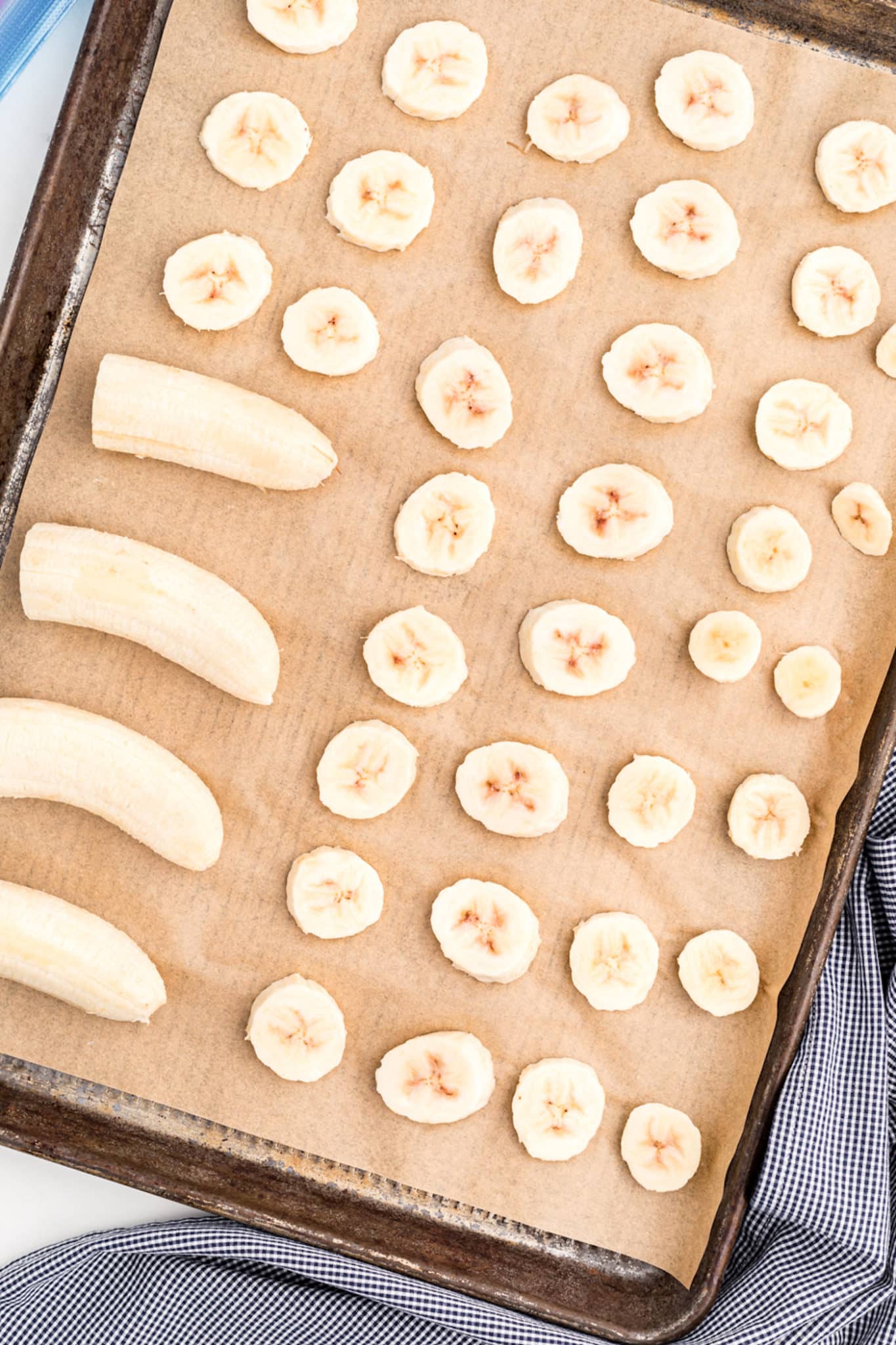 Banana halves and slices on a parchment-paper lined baking sheet.