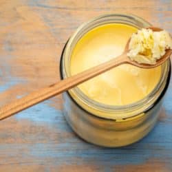 A wood spoon with a scoop of ghee over a full jar.