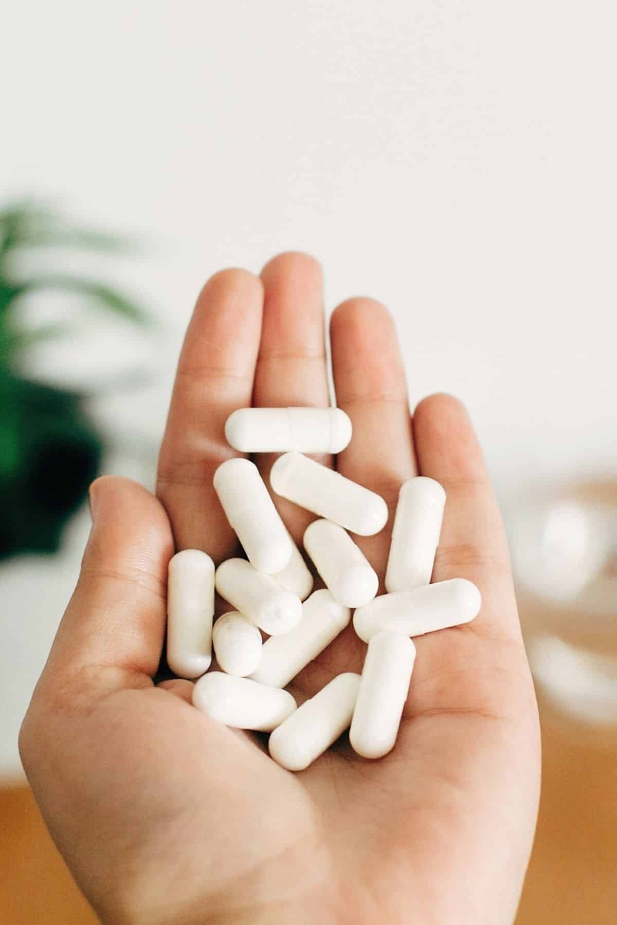 woman holding a handful of white magnesium capsules.