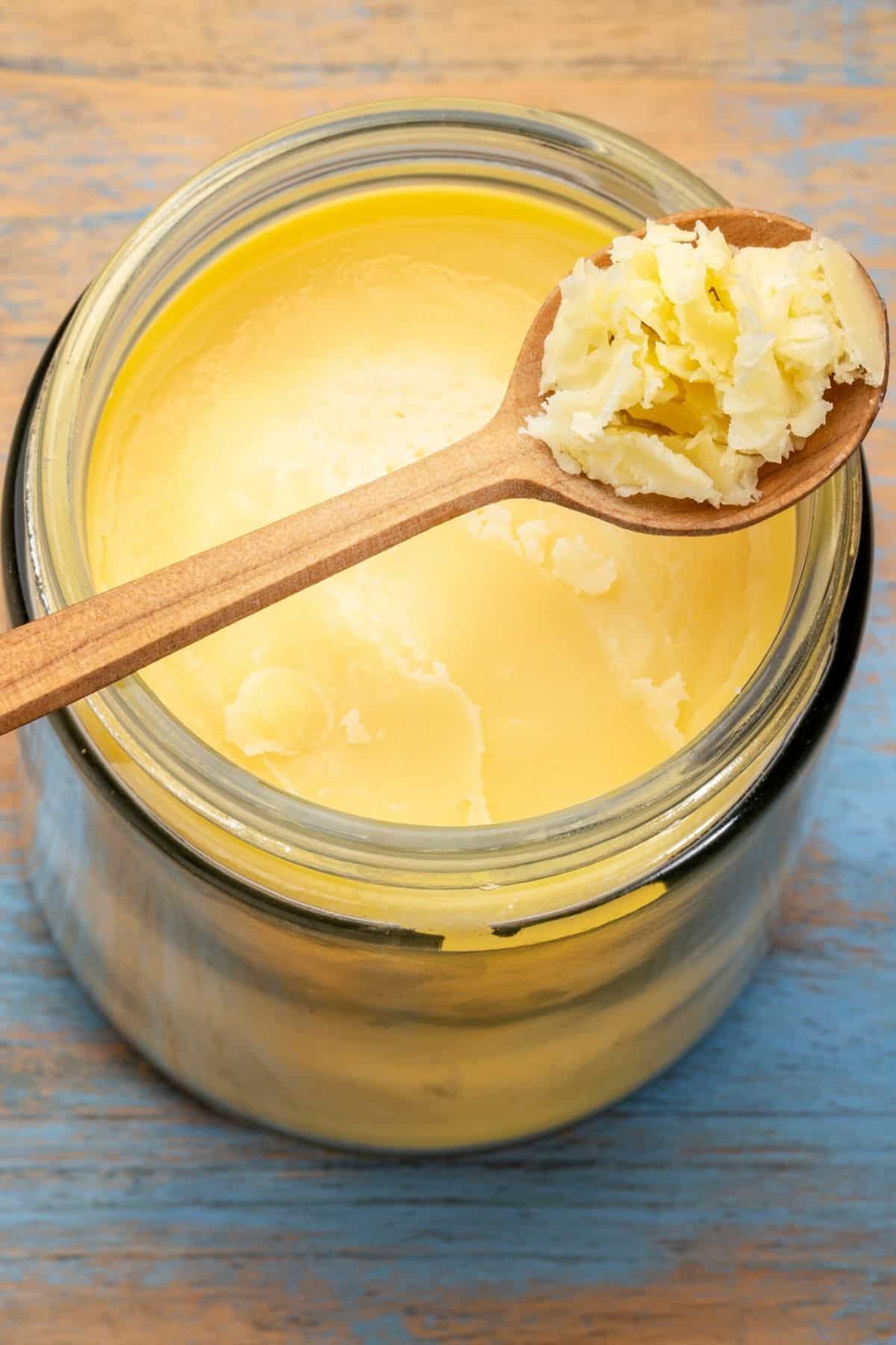 A wood spoon with a scoop of ghee over a full jar.