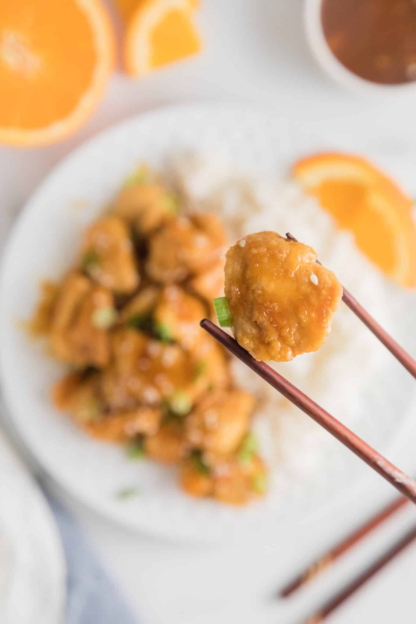 Chopsticks holding up a single bite of air fryer orange chicken.