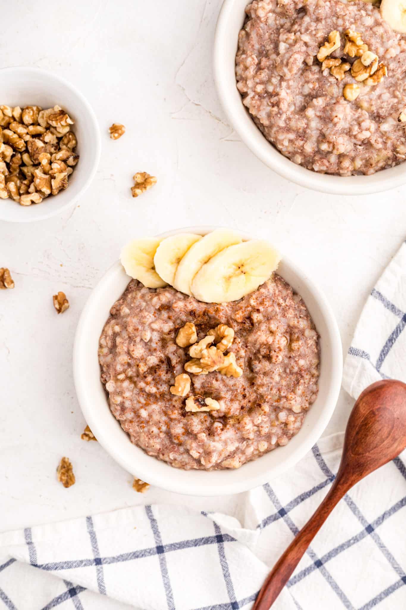 Two small bowls of buckwheat porridge topped with bananas and walnuts.