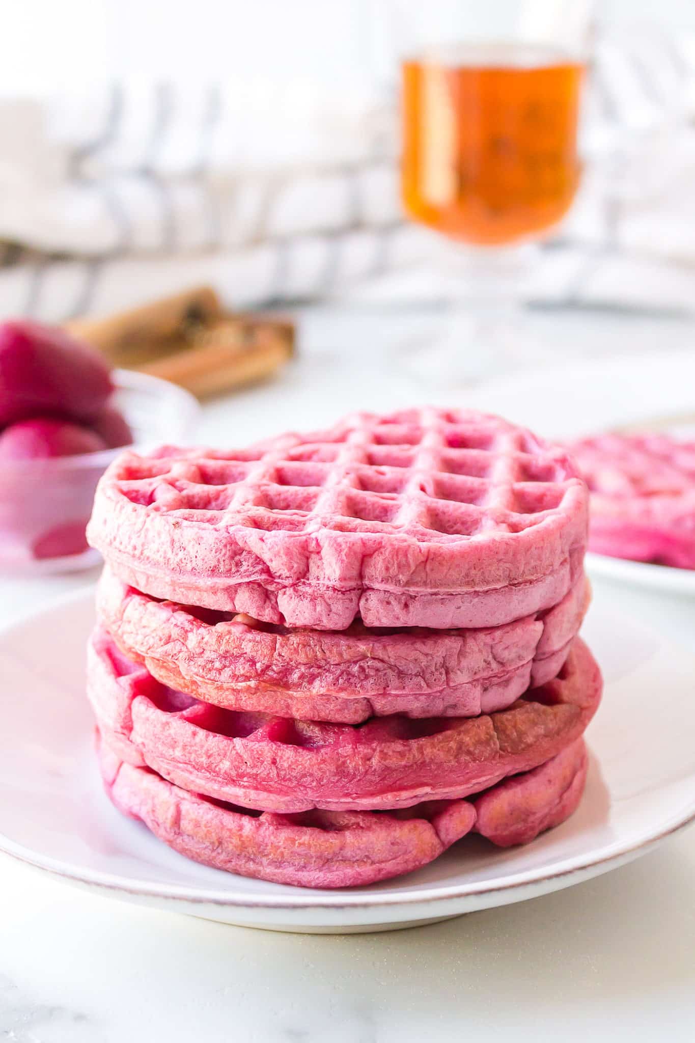 A stack of four pink waffles on a white plate.