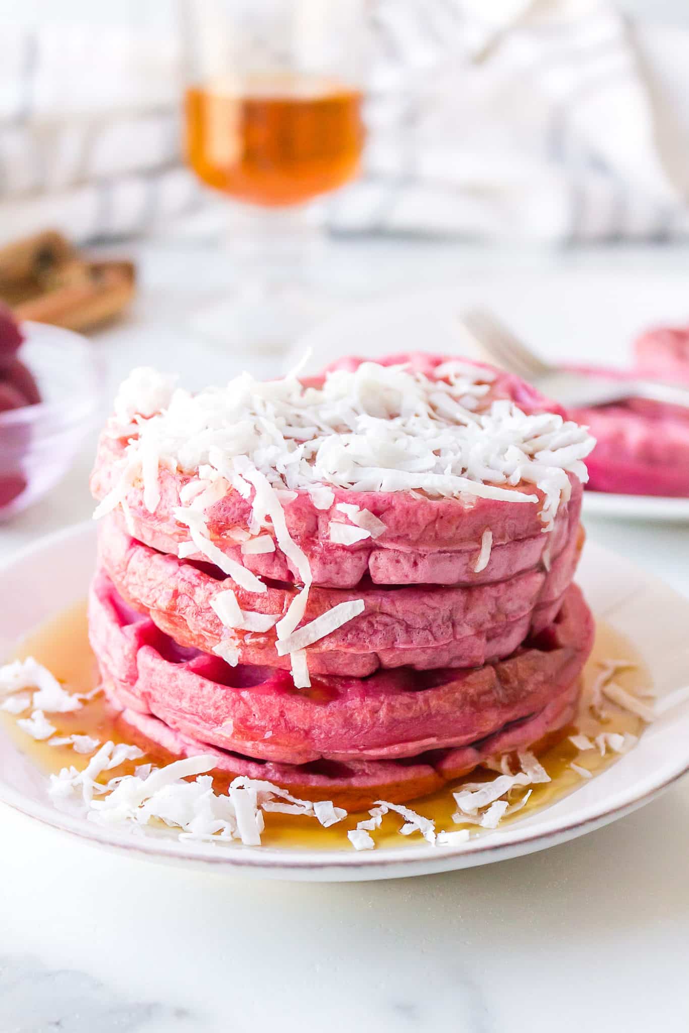 Shredded coconut and maple syrup on a stack of pink waffles on a plate.