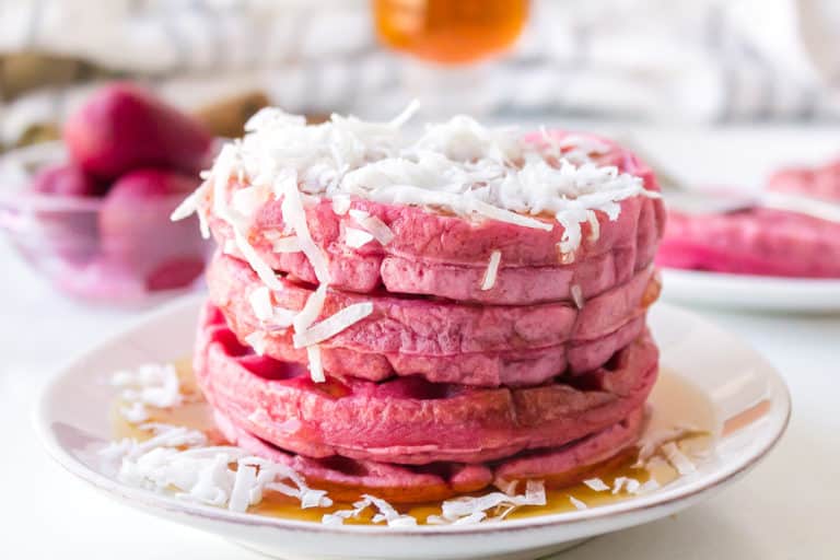 Shredded coconut and maple syrup on a stack of pink waffles on a plate.