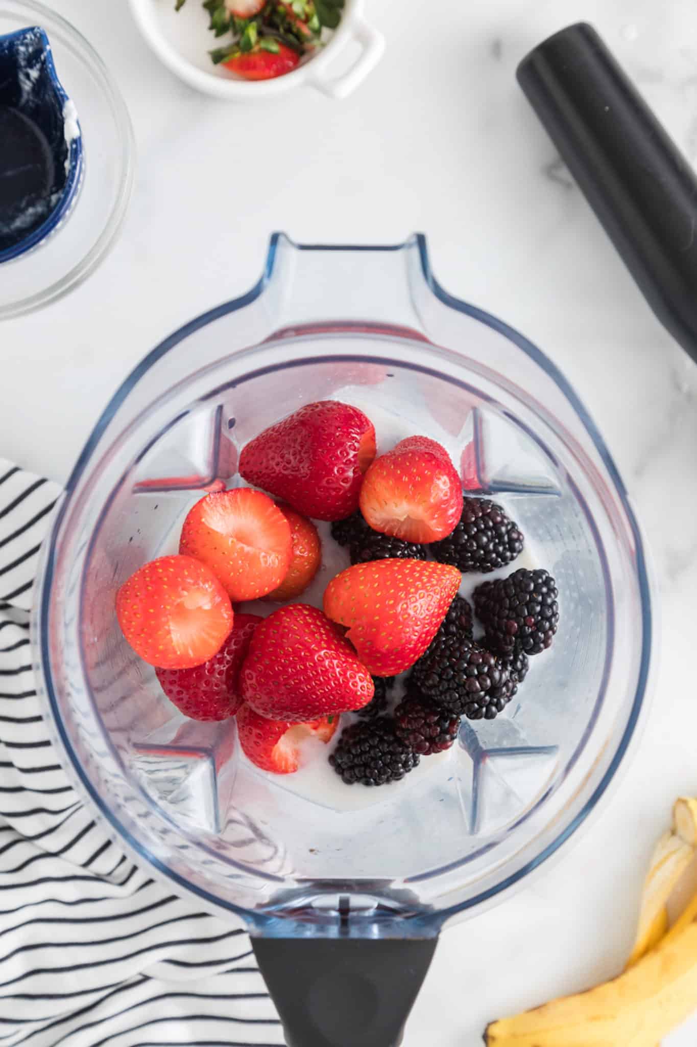 Fresh strawberries, blackberries, and milk in the jar of a blender.