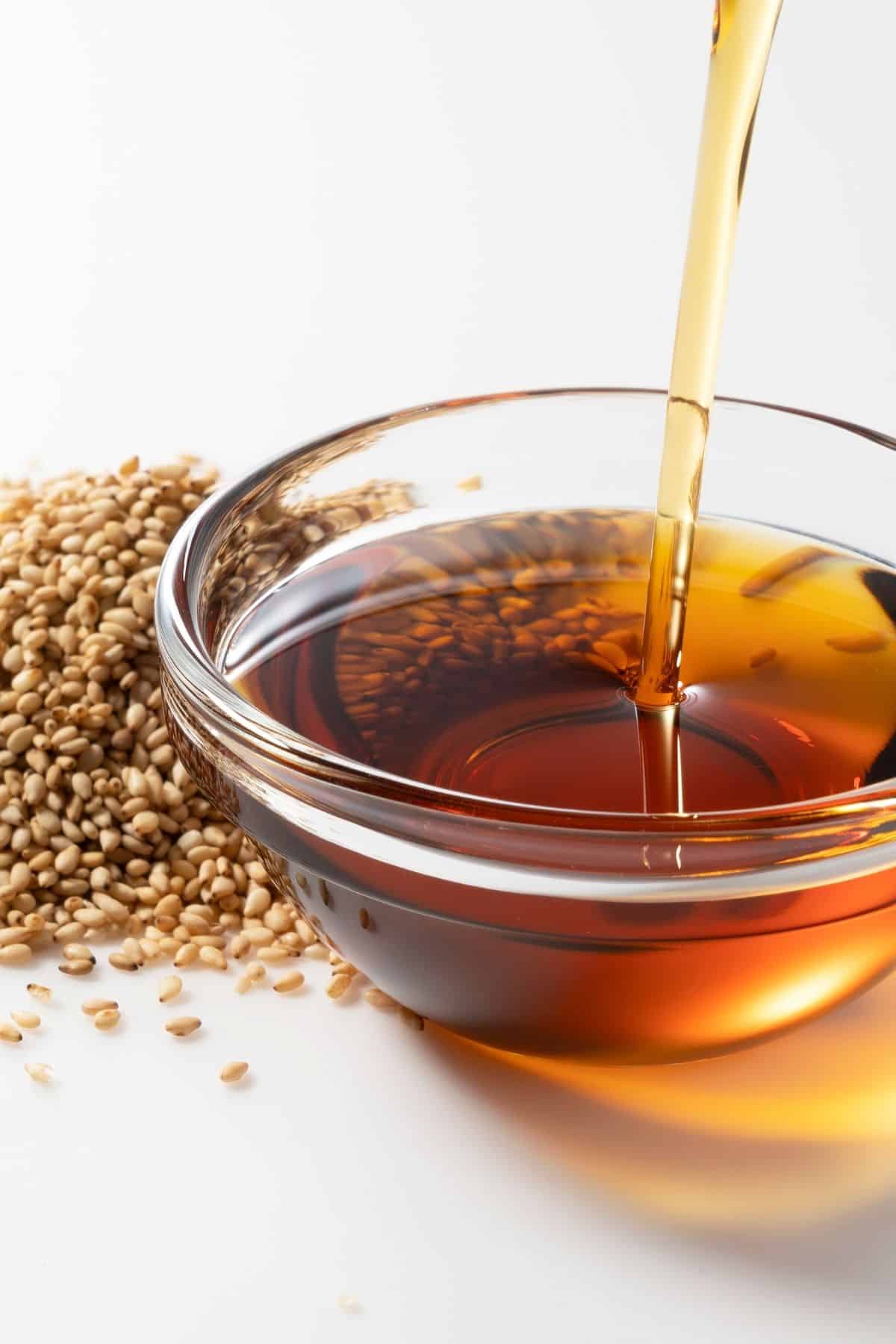 Small bowl of sesame oil next to sesame seeds on a counter.