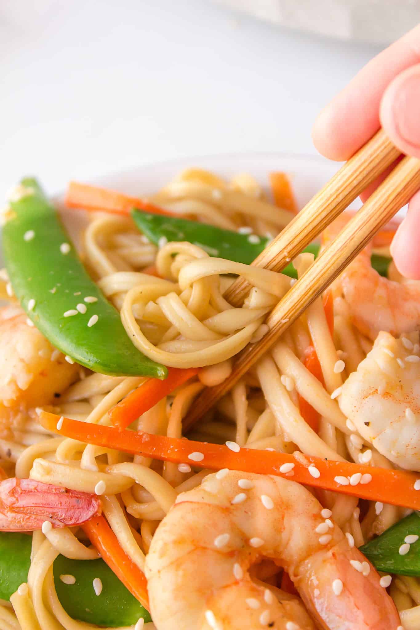 Chopsticks picking up shrimp udon noodles coated in sauce.