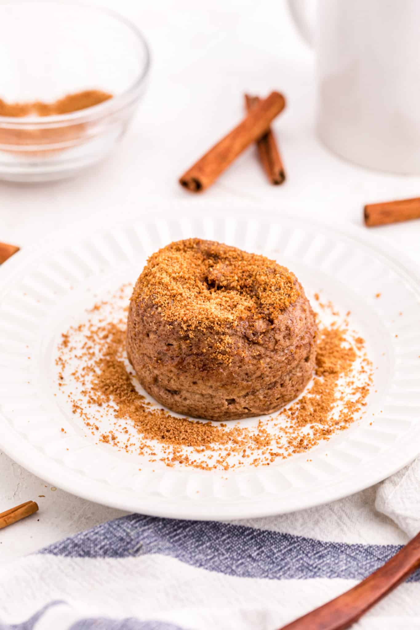A snickerdoodle mug cake set on a white plate and topped with cinnamon sugar.