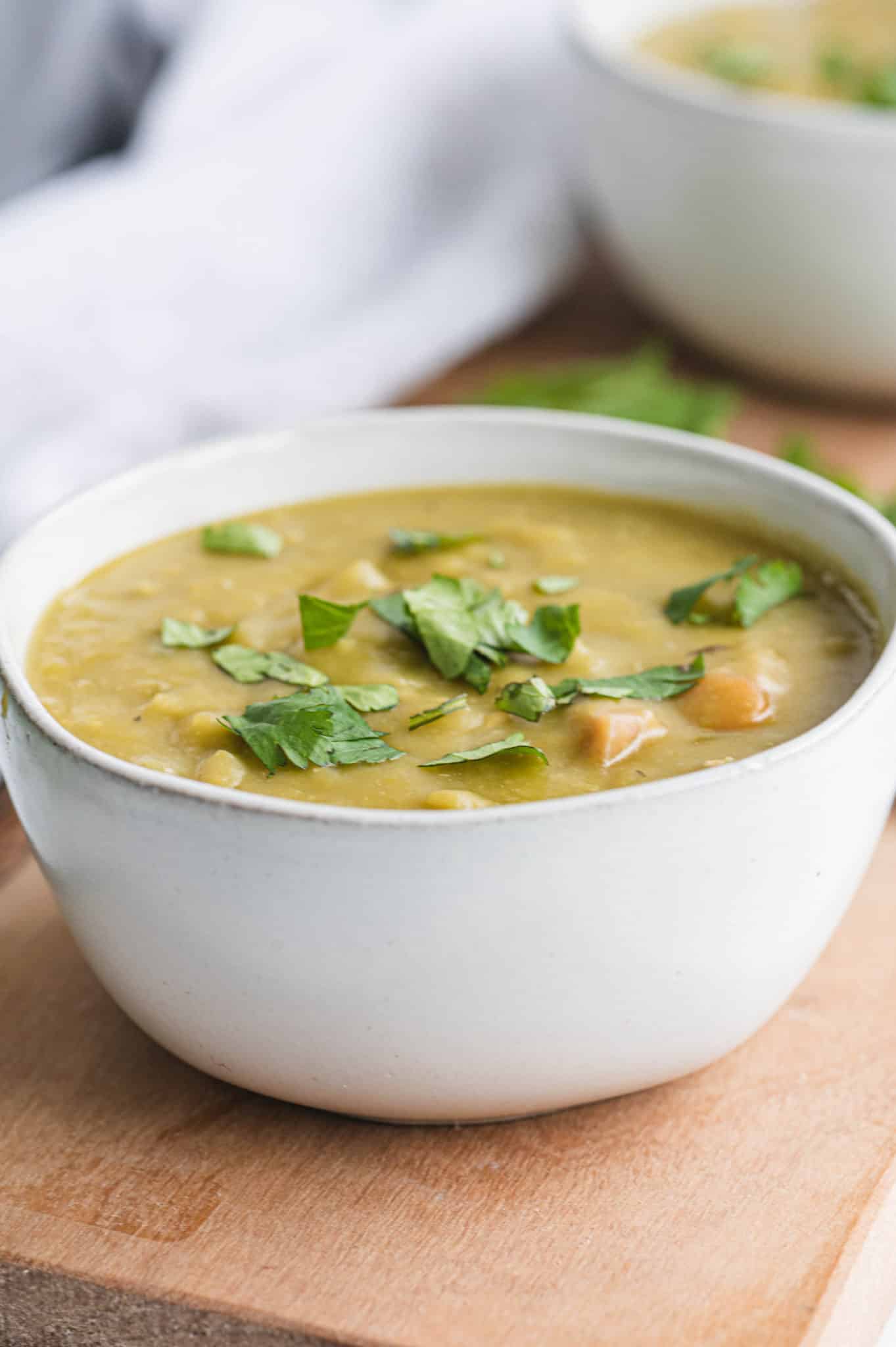 white ceramic bowl with a serving of split pea soup with chopped parsley on top.