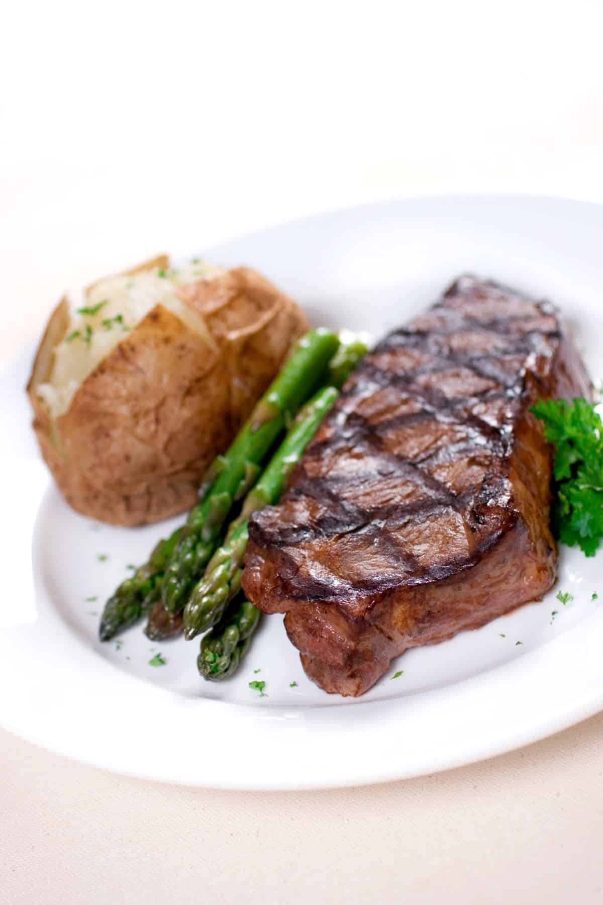 A plate of steak with a side of Baked potato and asparagus.