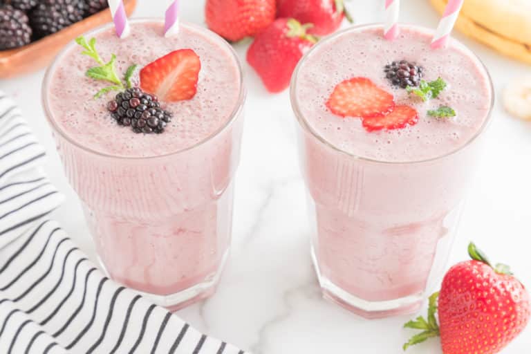 Two glasses of strawberry blackberry smoothie with fresh fruit and paper straws.