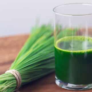 Wheatgrass juice in a glass next to a bundle of wheatgrass.