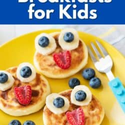 Pancakes with fruit faces on a yellow plate.