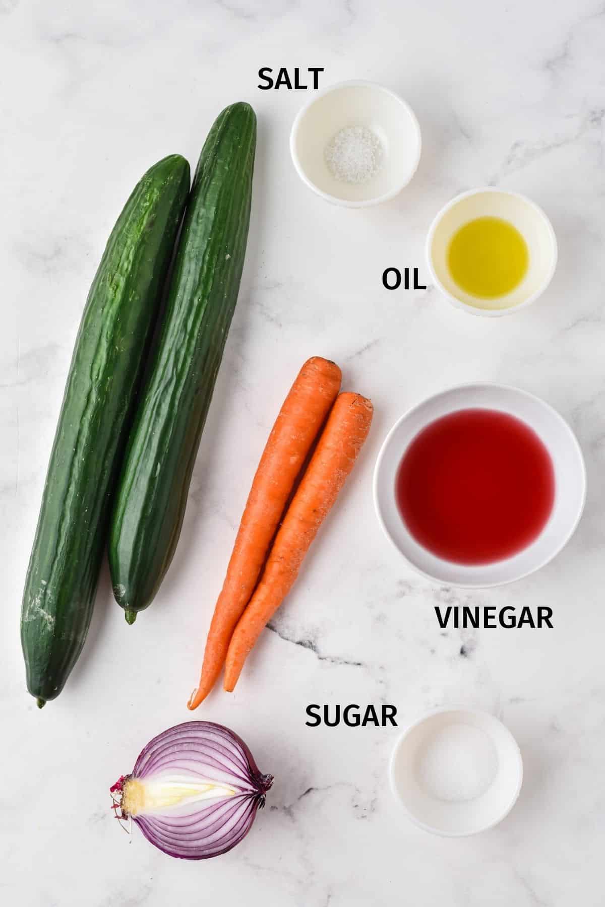 Ingredients for cucumber carrot salad in small bowls on a white surface.