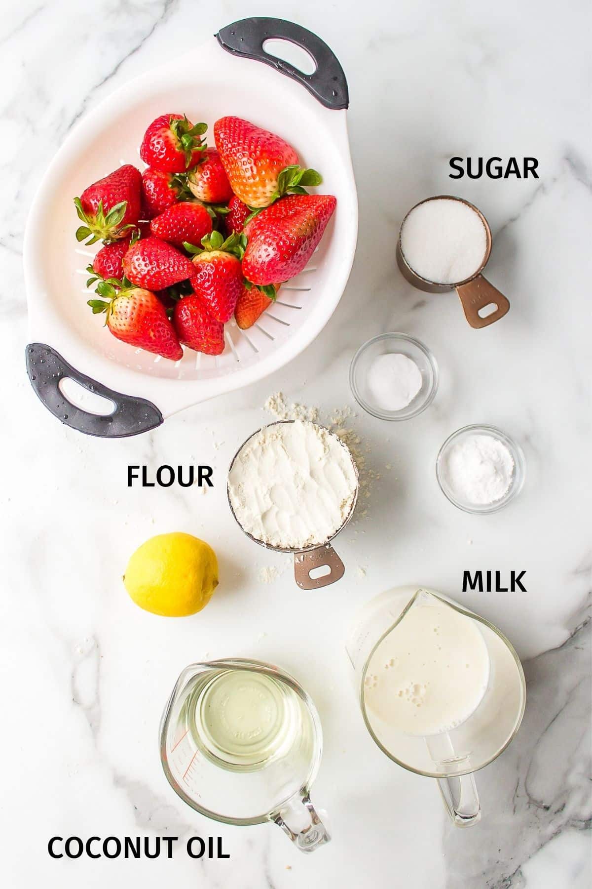 Ingredients for strawberry muffins in small bowls on a white surface.