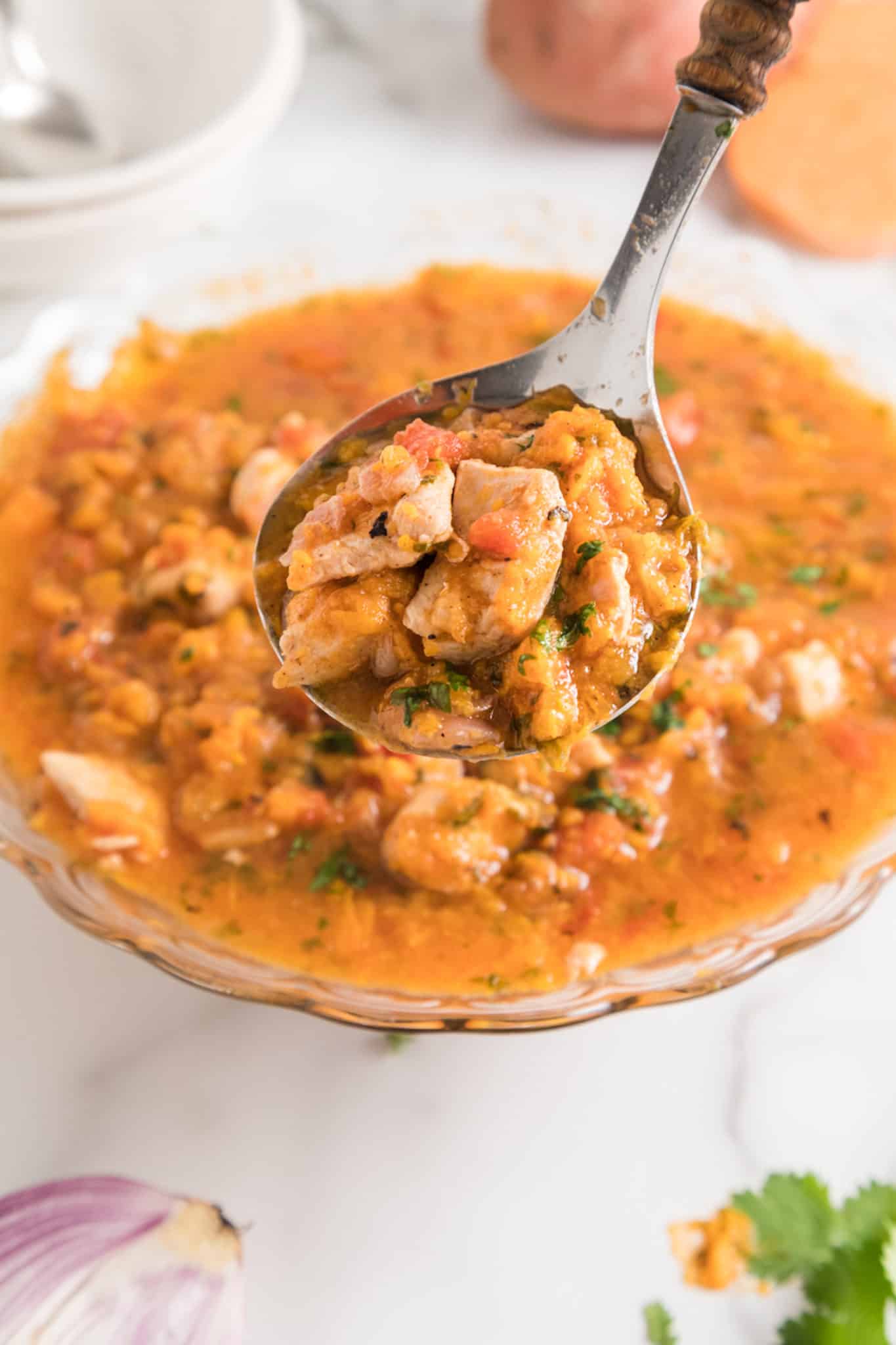 A spoonful of instant pot sweet potato chicken over a serving bowl.