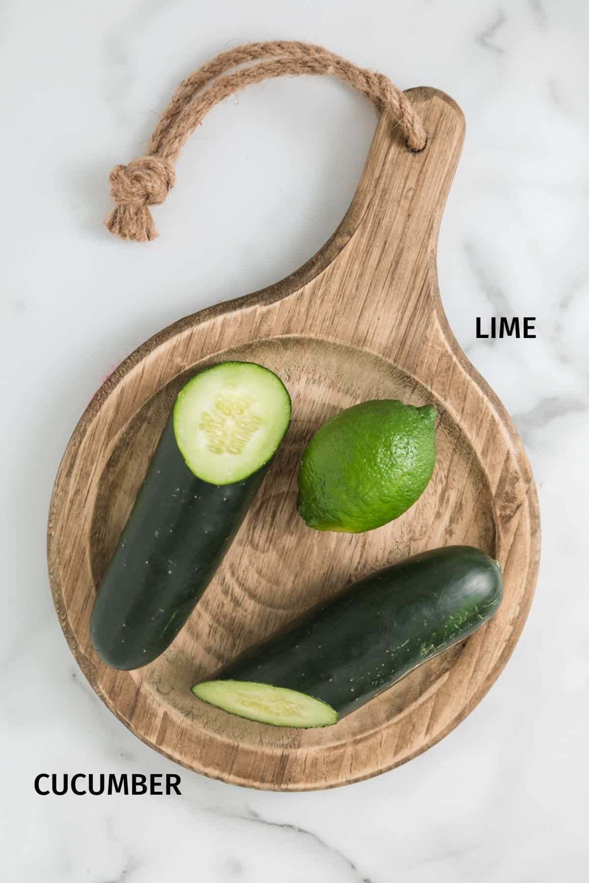 A lime and halved cucumber on a wood board.