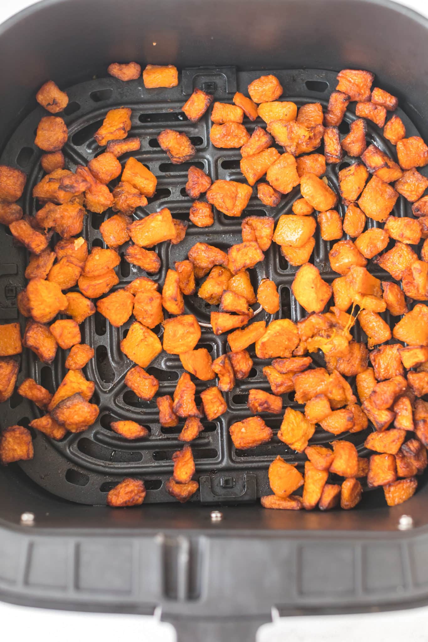 cooked butternut squash cubes in air fryer basket. 