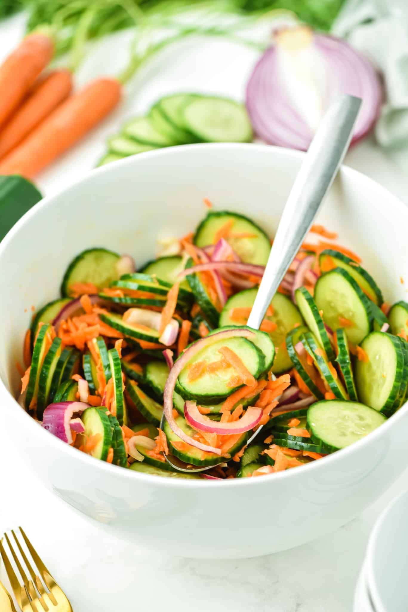 A forkful of cucumber carrot salad over a small white bowl full.