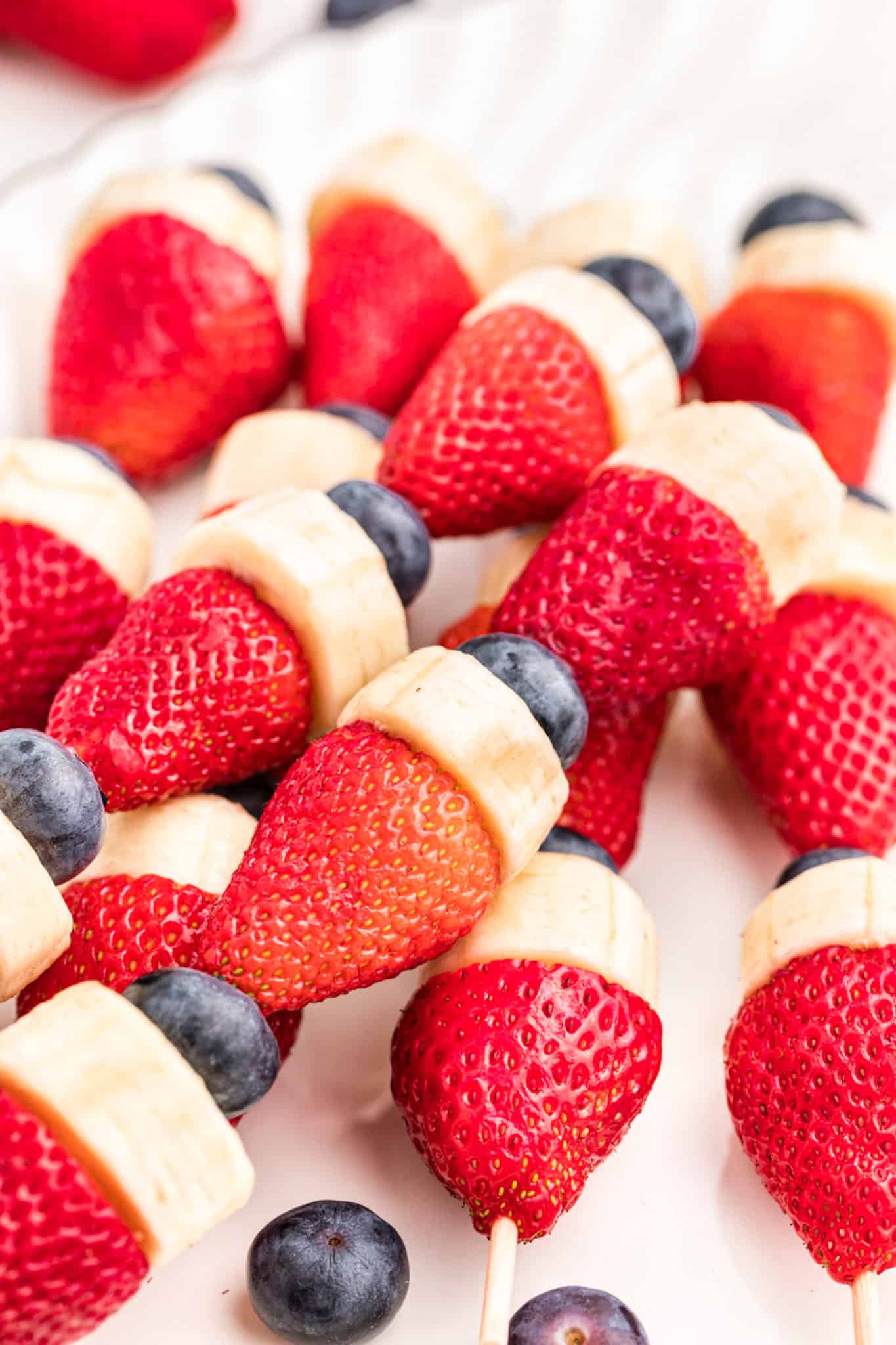 Closeup of patriotic strawberry fruit kabobs on a white surface.