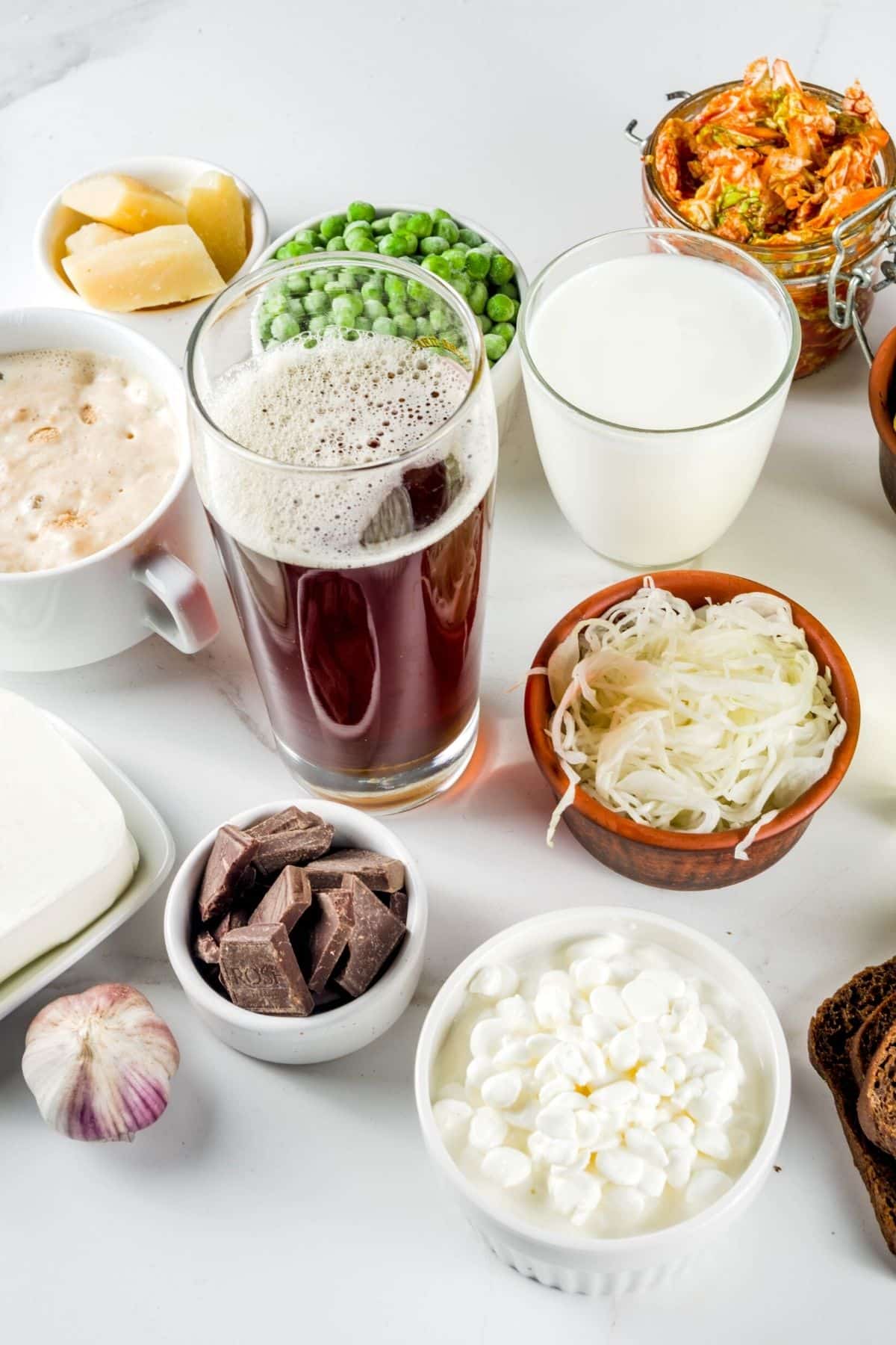 Various gut healing foods in glasses and bowls on a white surface.