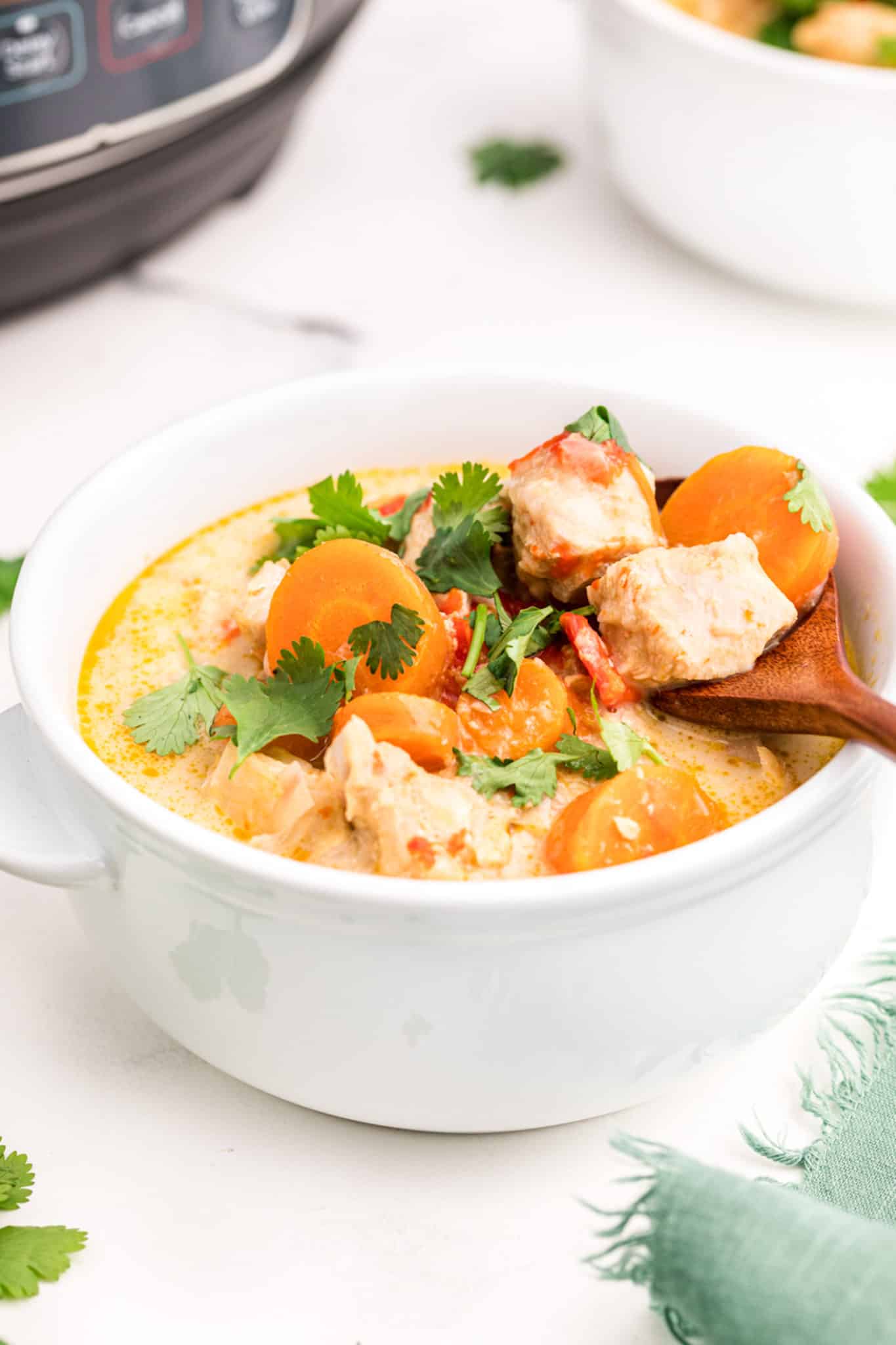 A wooden spoon in a small white bowl of Thai Chicken Curry Soup.